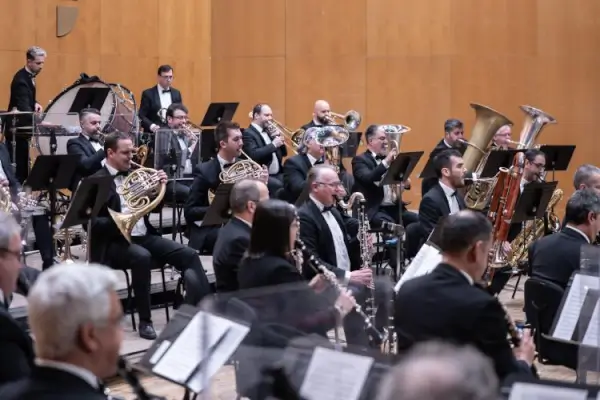 Músicos tocando instrumentos tradicionales gallegos como la gaita y la zanfona junto a una banda sinfónica en un escenario al aire libre.