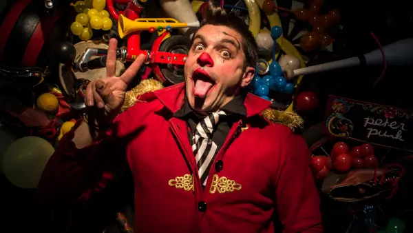 Peter Punk, un payaso con vestuario colorido, realiza un acto de circo con malabares y expresiones cómicas en el escenario.
