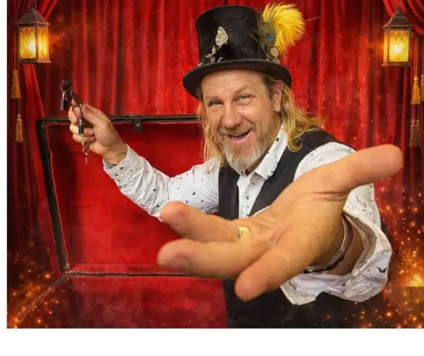 El Mago Midas, sonriente, realiza un truco de magia con una baraja de cartas en un escenario que simula un museo antiguo.