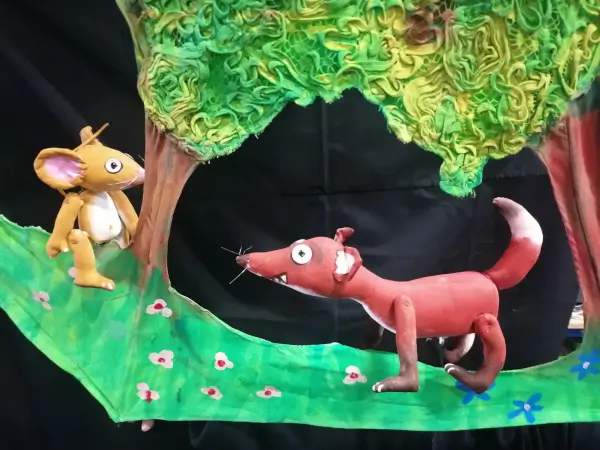 Un ratón de títere astuto frente a un zorro, un mochuelo y una serpiente, todos títeres, en un escenario que representa un bosque.