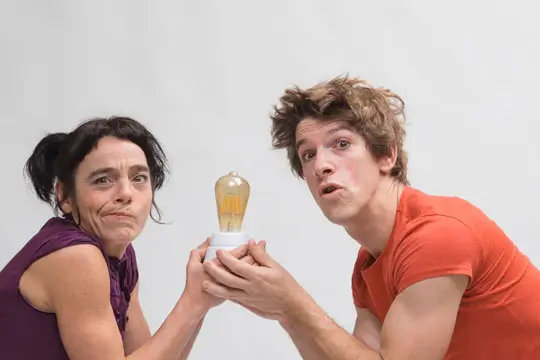 Dos artistas de circo realizando acrobacias aéreas y malabares en un escenario minimalista.