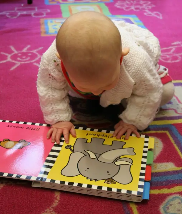 Una mujer sonriente narrando un cuento a un grupo de bebés y sus padres sentados en el suelo de una biblioteca.