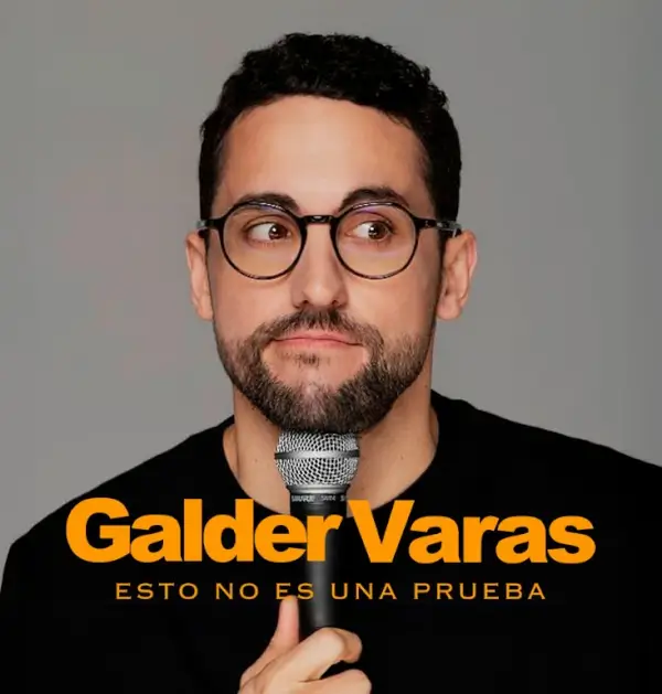 El cómico Galder Varas en el escenario durante una actuación de monólogo, con un micrófono y un fondo oscuro.