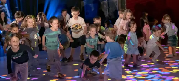 Niños y bailarines de Brodas Bros en un escenario colorido, bailando breakdance y mostrando elementos de grafiti.
