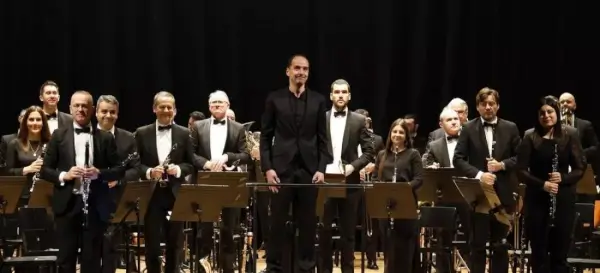 Miembros de la Banda Municipal de Música de Santiago de Compostela interpretando sus instrumentos en un escenario iluminado.