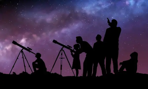 Personas observando el cielo nocturno a través de un telescopio portátil frente a una biblioteca.